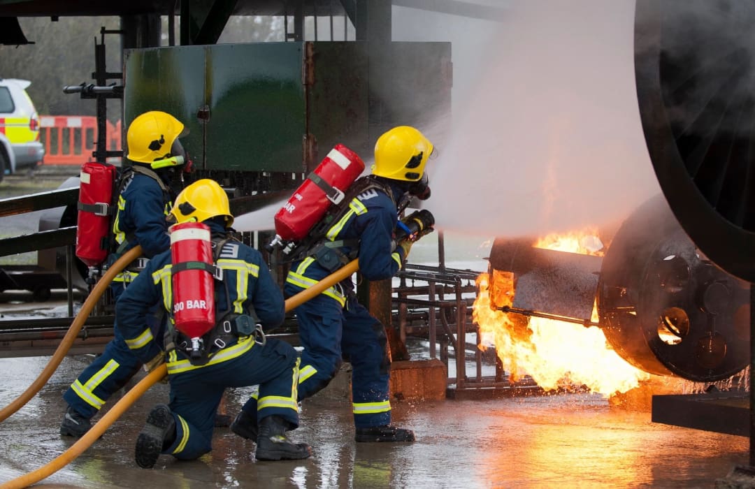 A group of people in yellow helmets are using fire hoses to put out a car on fire.